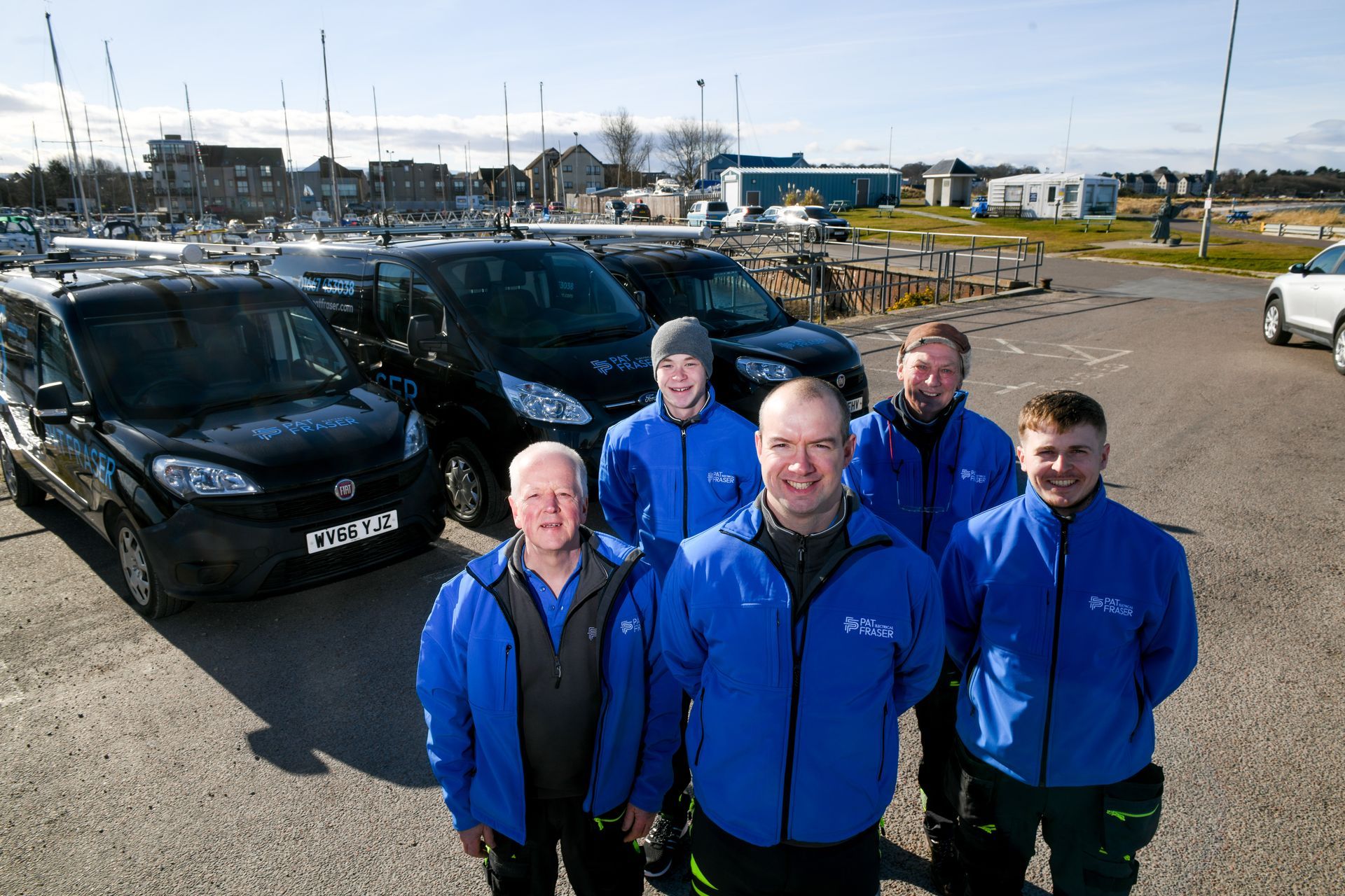 A group of men in blue jackets are standing in front of a row of black vans.