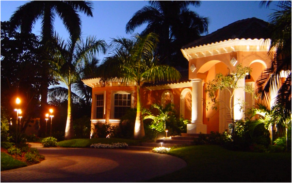 A house is lit up at night with palm trees in the background