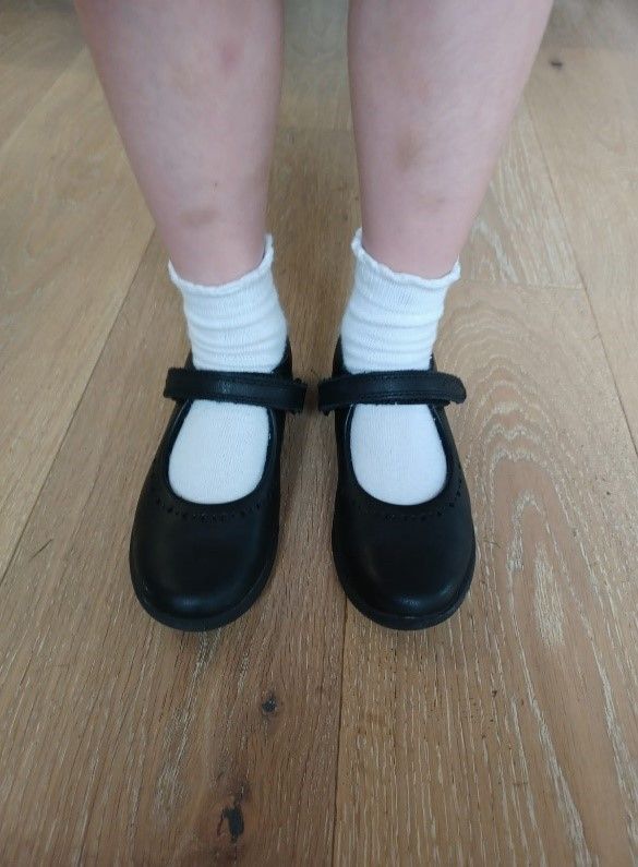 A person wearing black shoes and white socks is standing on a wooden floor.
