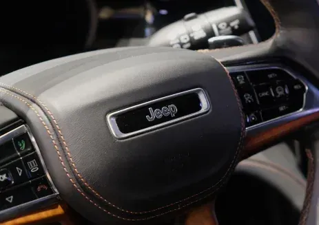 A close-up of a Jeep steering wheel with a leather-wrapped center featuring the Jeep logo and mounted control buttons.