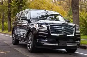 A black Lincoln Navigator SUV parked on an asphalt road with trees in the background.