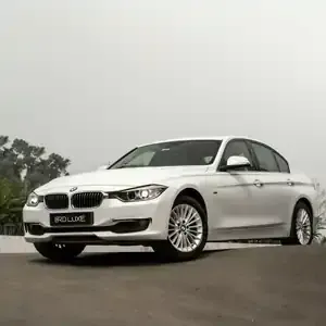A white BMW 3 Series sedan parked on an asphalt slope against a soft, overcast sky.