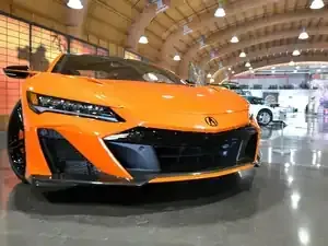 A bright orange Acura NSX parked on a polished concrete floor inside a large, arched-ceiling showroom.