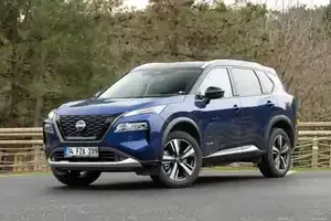 A blue Nissan X-Trail SUV parked on an asphalt road in front of trees.