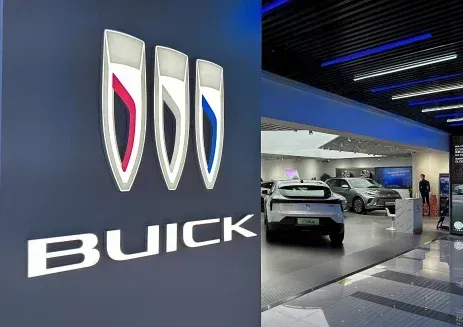 The Buick logo featuring three shields in red, silver, and blue, with a car dealership showroom visible in the background.