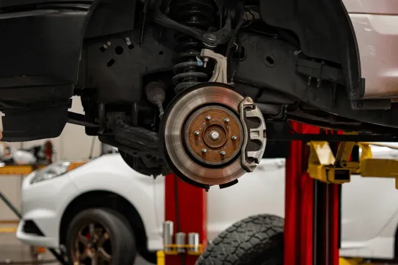 The front wheel assembly and brake rotor of a vehicle hoisted on a lift in an auto repair shop.