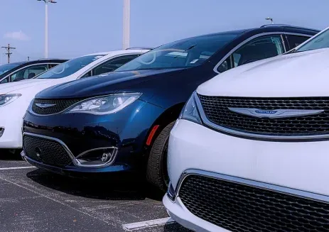 A row of Chrysler cars parked on an outdoor lot, featuring a blue vehicle between two white ones.