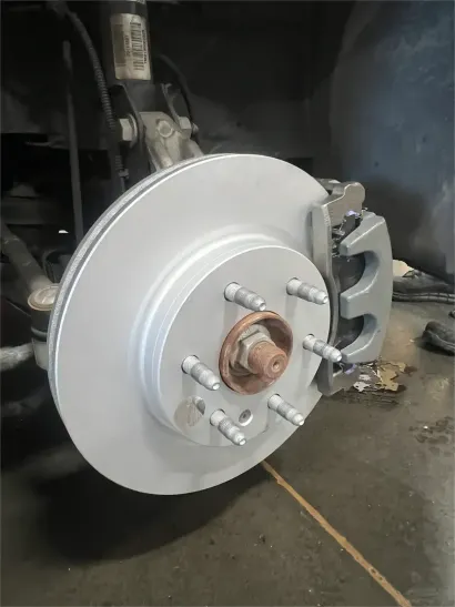 Close-up of a car's exposed rear brake rotor and suspension on a lift in a garage