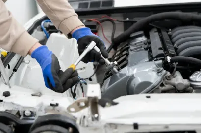 A person wearing blue and black work gloves uses a ratchet to work on a car engine.