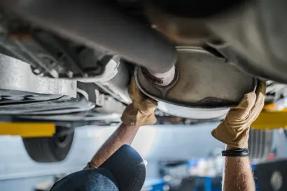 A technician in work gloves inspecting or repairing the muffler of a car lifted on a garage rack.