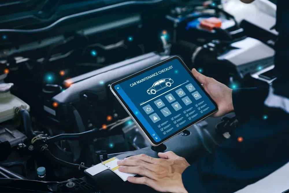 A mechanic uses a tablet displaying a car maintenance checklist while inspecting a vehicle's engine.