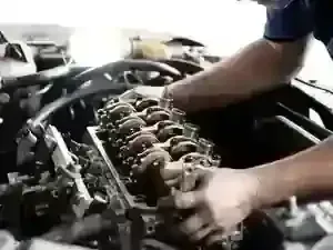 Mechanic working on the open engine block of a car, adjusting metal components under bright lighting.