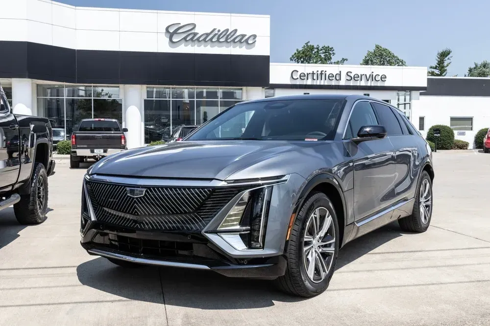 A dark gray Cadillac Lyriq parked in front of a Cadillac dealership on a sunny day.