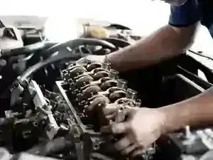 A mechanic working on the exposed valve train of an open car engine in a repair shop.