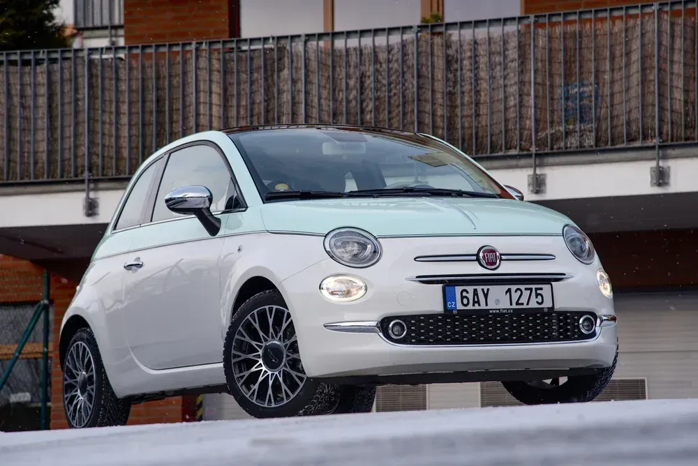 A two-toned white and mint green Fiat 500 parked on a paved surface in front of a modern building.