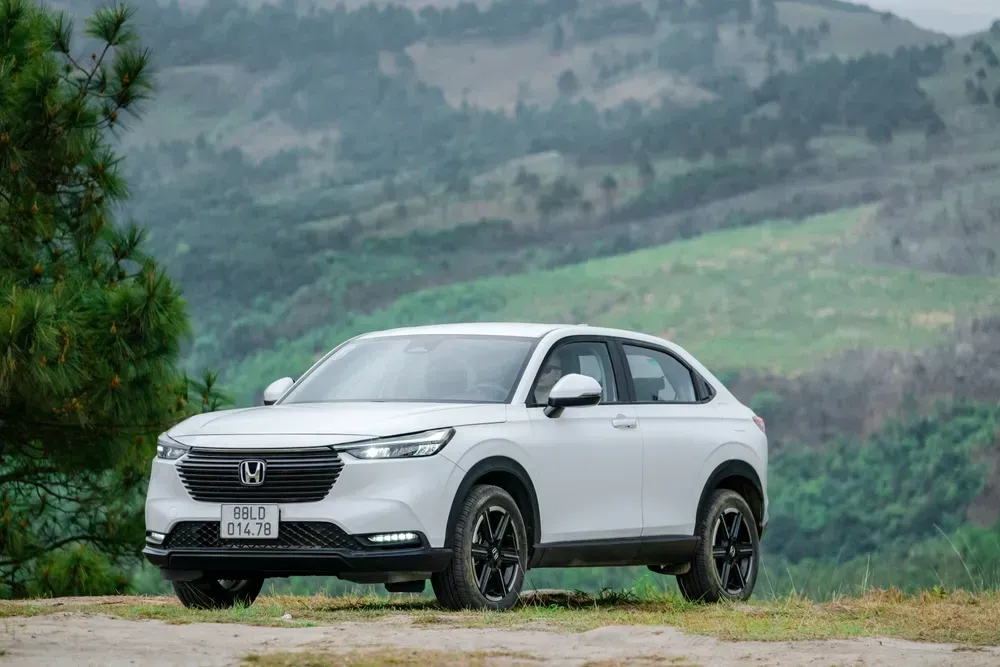 A white Honda HR-V SUV parked on a dirt path against a backdrop of rolling green hills.