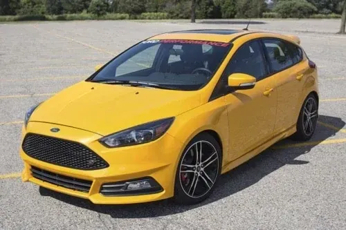 A yellow Ford Focus ST hatchback parked in a large, empty paved lot.