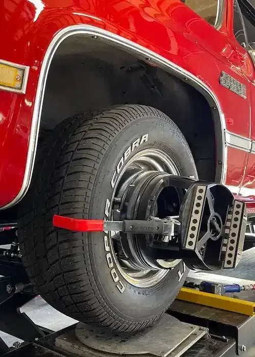 A sensor from an alignment machine attached to the tire of a bright red vehicle in a repair shop.