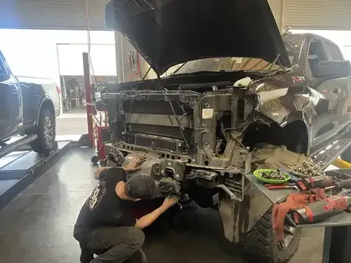 A mechanic works on the front end of a disassembled pickup truck inside an auto repair shop.