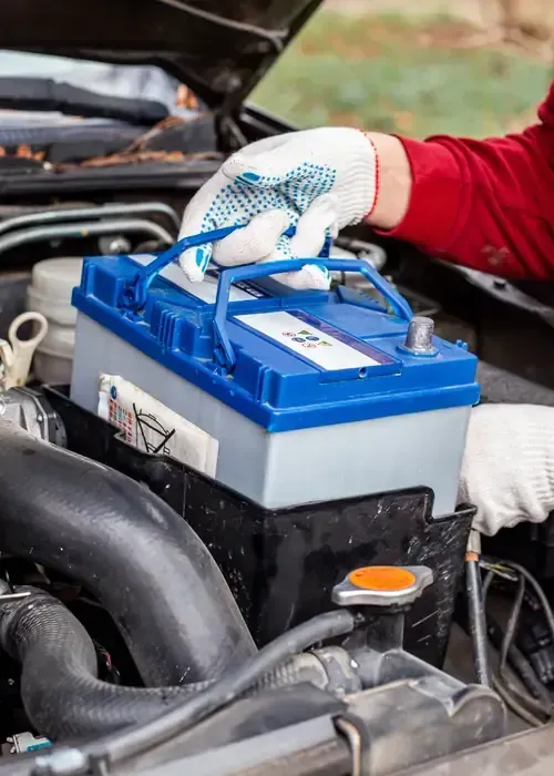 A person wearing gloves places a blue and grey car battery into the engine bay of a vehicle.