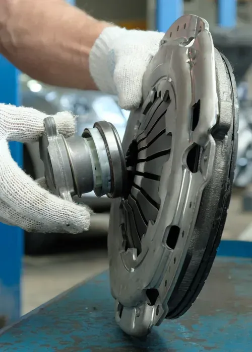 Hands in white gloves holding a metal automotive clutch release bearing against a vehicle clutch pressure plate.
