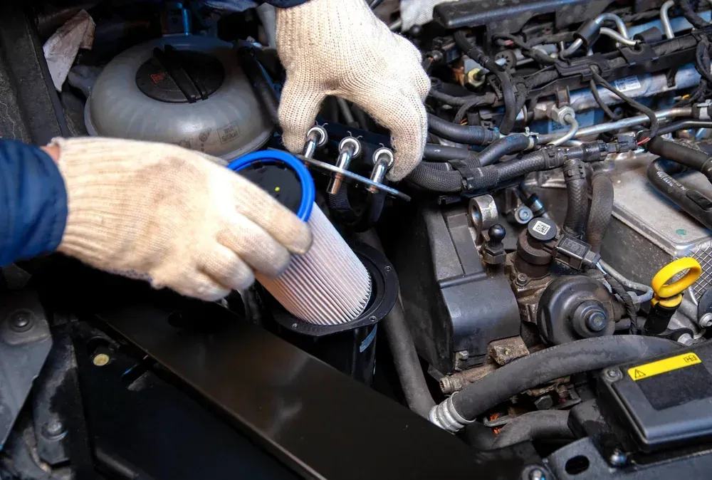 Golden motor oil pouring from a blue plastic bottle into an open engine oil filler cap.
