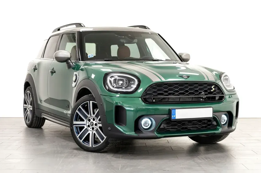 A British racing green Mini Countryman SUV with silver stripes parked in a bright, white-walled studio.