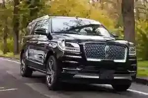 A black Lincoln Navigator SUV parked on an asphalt road with trees in the background.