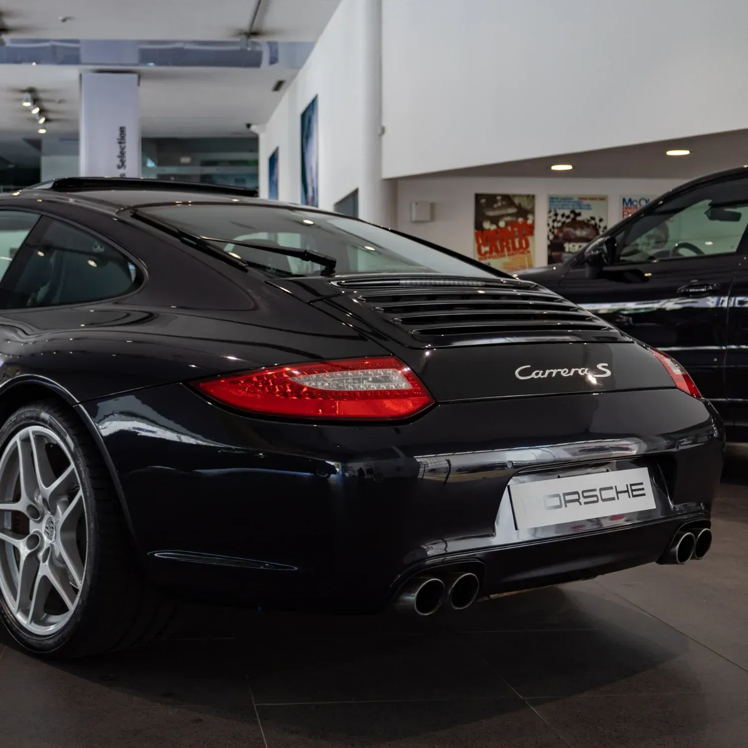 A dark, shiny Porsche Carrera S parked inside a bright car dealership showroom.