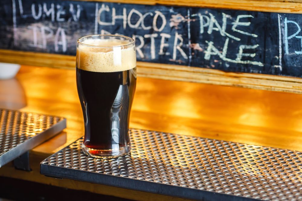 Glass of Dark Beer on a Metal Bar With a Chalkboard Menu — Capricorn Tavern in Taranganba, QLD