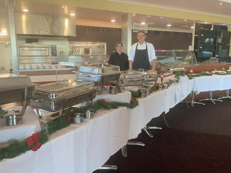 Two People Standing Behind a Buffet Table With Chafing Dishes — Capricorn Tavern in Taranganba, QLD