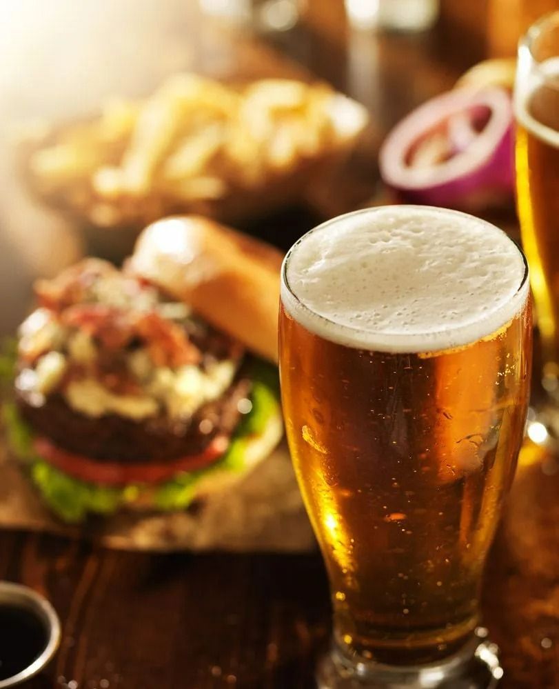 A Glass of Beer With a Foamy Head, a Burger, and Fries on a Wooden Table — Capricorn Tavern in Taranganba, QLD