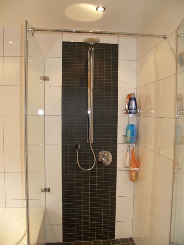 Eine Dusche mit einer schwarz gefliesten Wand und einer Glastür