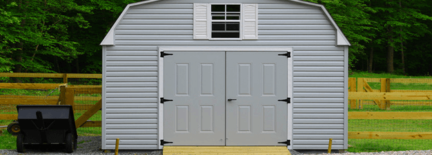 A white barn is sitting in the middle of a grassy field next to a wooden fence.