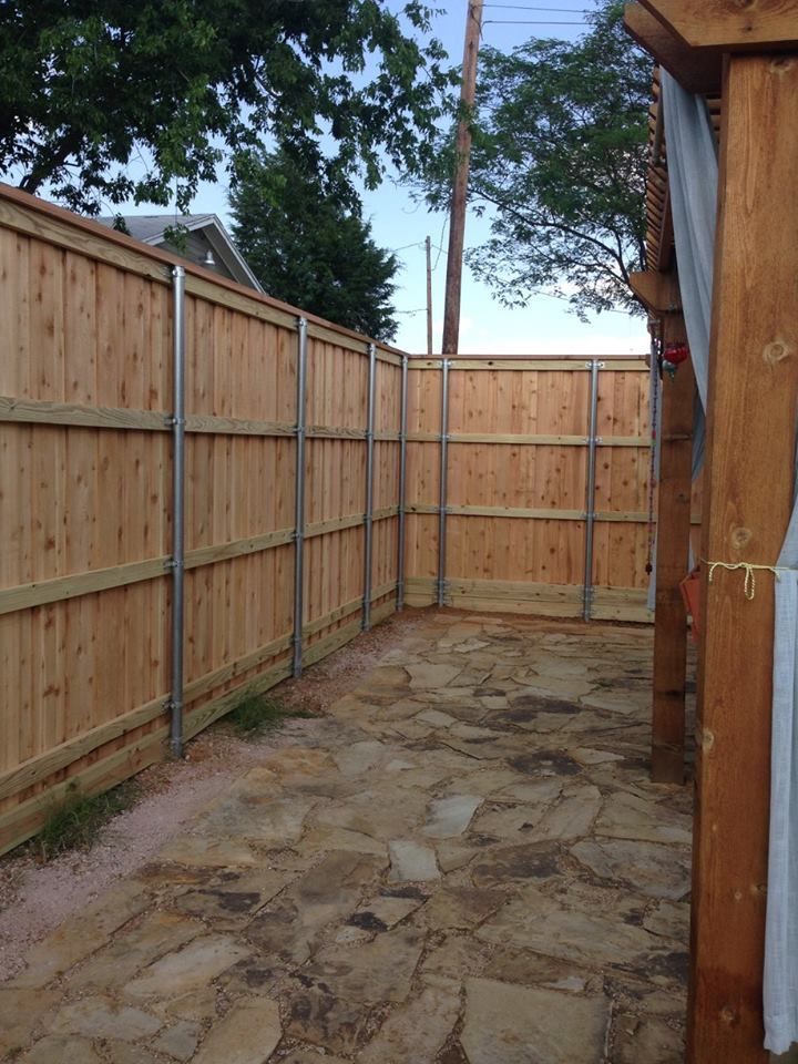 A wooden fence surrounds a stone patio with trees in the background