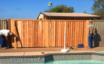 Two men are working on a wooden fence next to a pool.