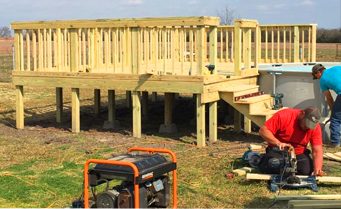 Two men are working on a wooden deck next to a pool.