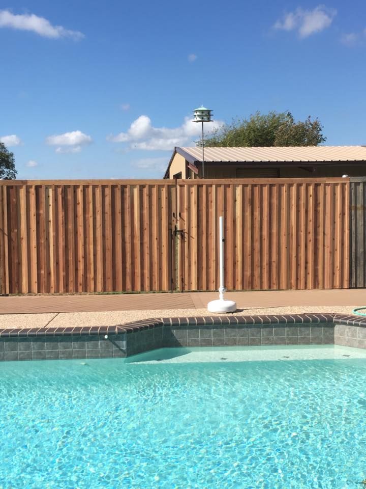 A wooden fence surrounds a swimming pool on a sunny day