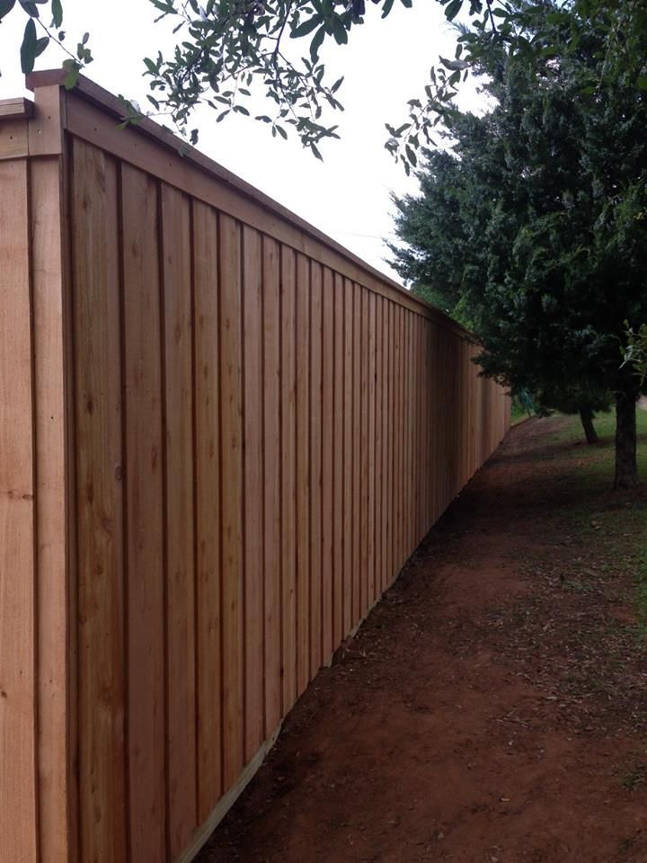 A wooden fence along a dirt path surrounded by trees