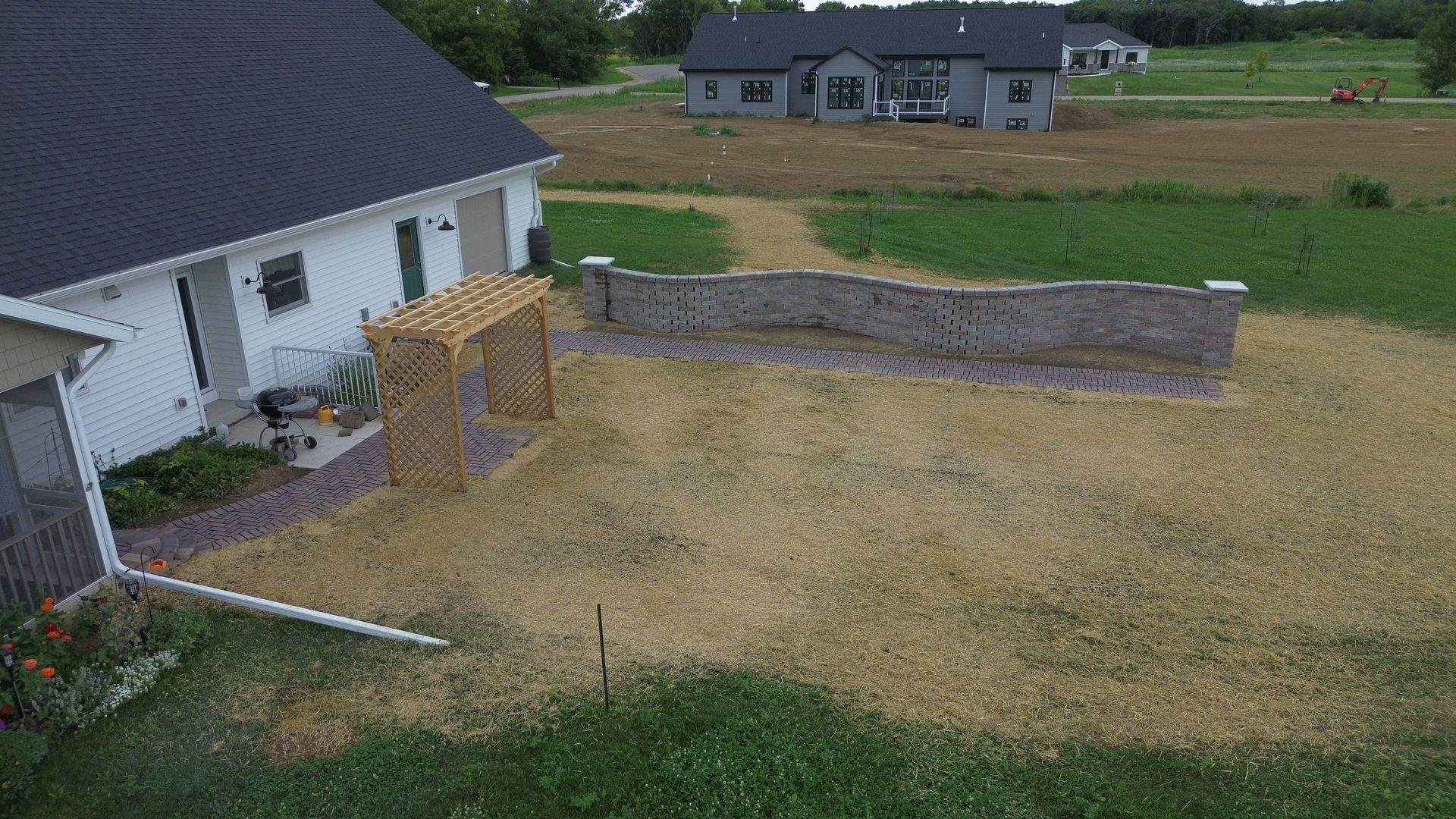 Backyard with a white house, wooden deck, stone retaining wall, and fenced grassy yard