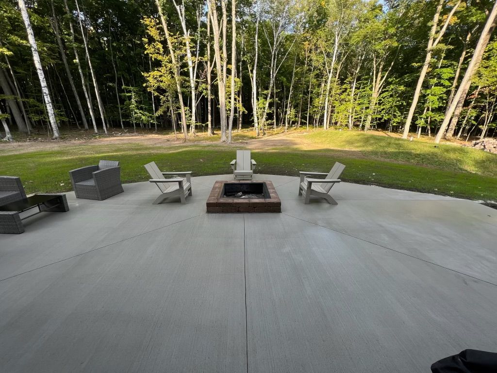 Patio with fire pit and lounge chairs overlooking a grassy yard and wooded trees
