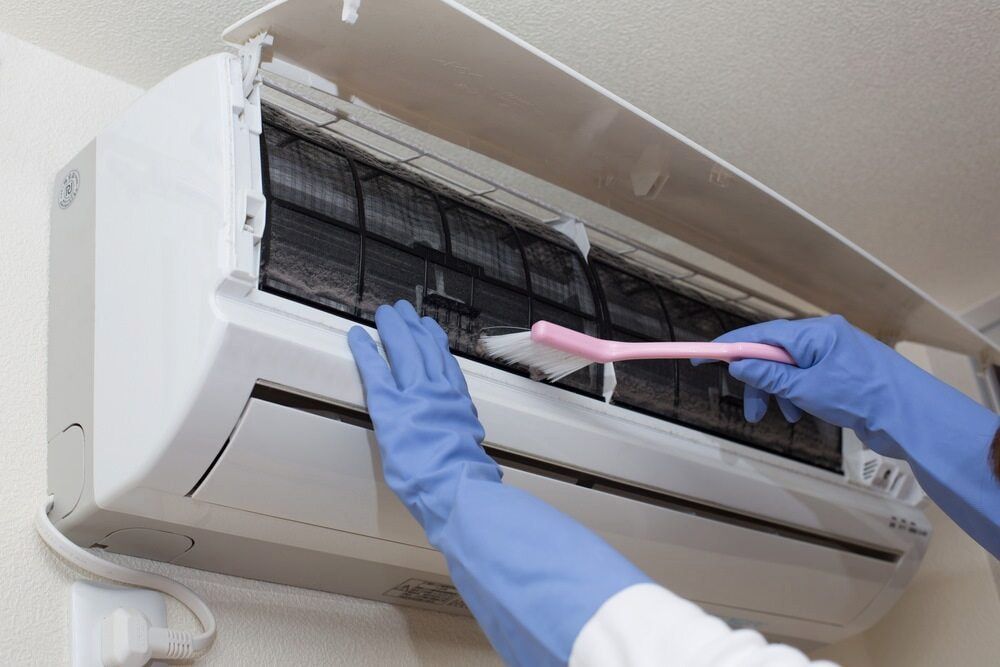 Person in Blue Gloves Cleaning an Air Conditioner Filter With a Pink Brush — EcoAir Airconditioning in Zuccoli, NT