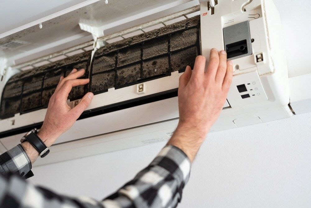 Person Removing a Dirty Air Filter From a White Air Conditioning Unit Mounted — EcoAir Airconditioning in Palmerston, NT