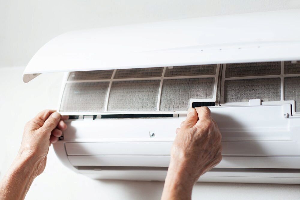 Hands removing a dusty air filter from a white air conditioner unit on a wall. — EcoAir Airconditioning in Zuccoli, NT