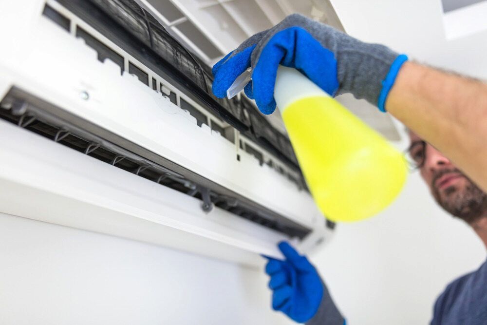 Person wearing blue gloves sprays cleaning solution on an air conditioning unit. — EcoAir Conditioning in Palmerston, NT