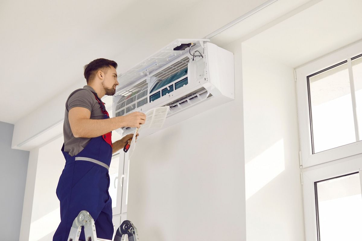 Man on Ladder Repairing an Air Conditioner Unit Mounted — EcoAir Airconditioning in Humpty Doo, NT