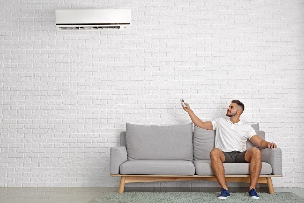 Man Sitting on a Gray Sofa, Using a Remote to Control an Air Conditioner — EcoAir Conditioning in Coconut Grove, NT