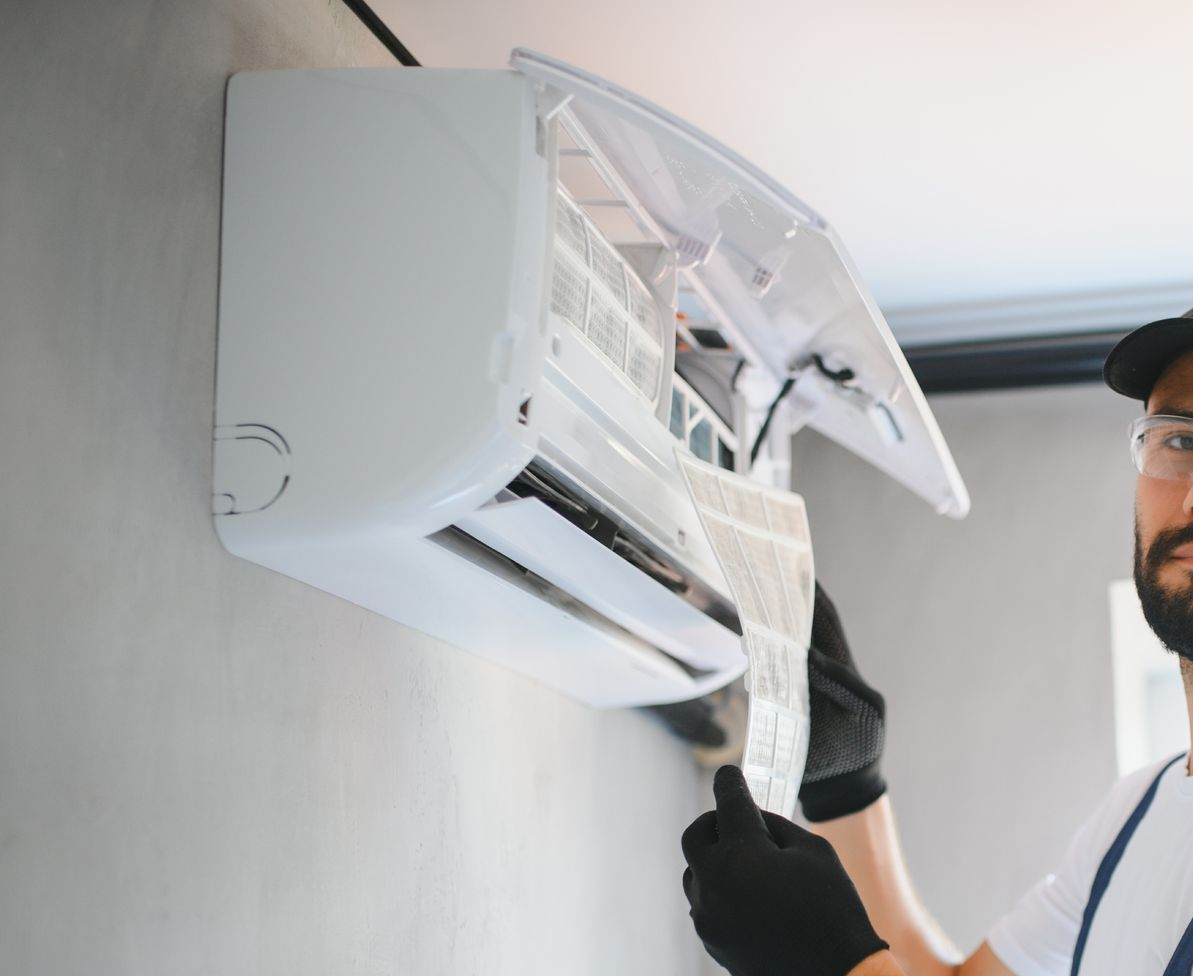 A technician in gloves removes a filter from a wall-mounted air conditioning unit for maintenance. — EcoAir Conditioning in Coconut Grove, NT