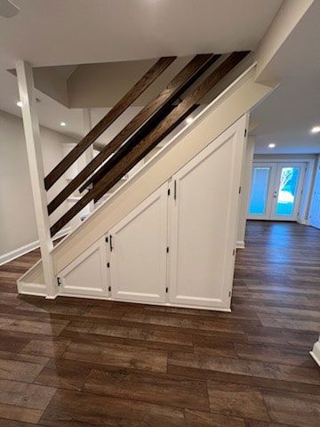 White cabinetry built under a staircase, brown wood floor, dark wooden stair railing.