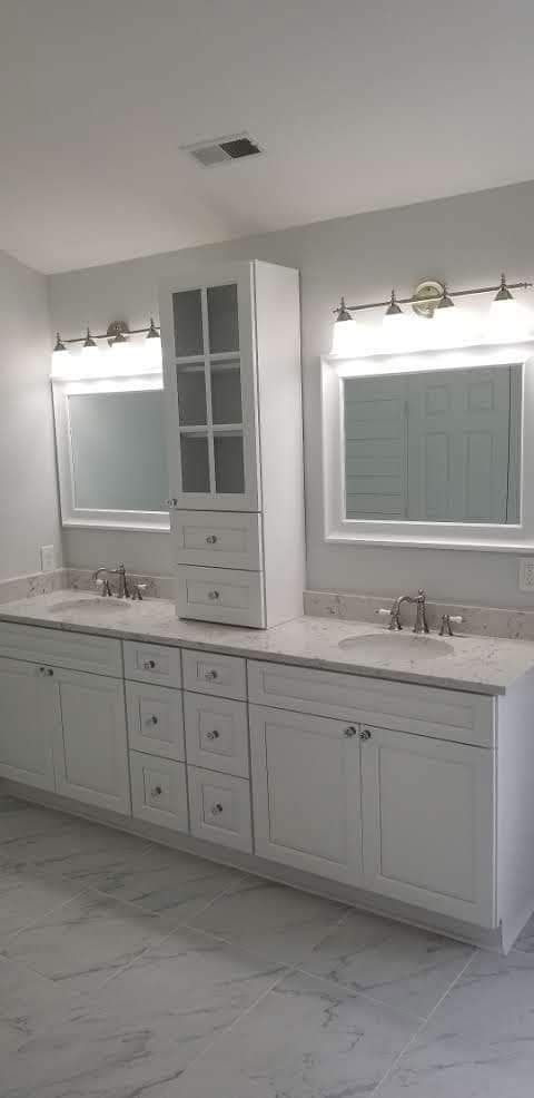 White bathroom vanity with two sinks, mirrors, and a tall cabinet. Light-colored countertops and tile flooring.